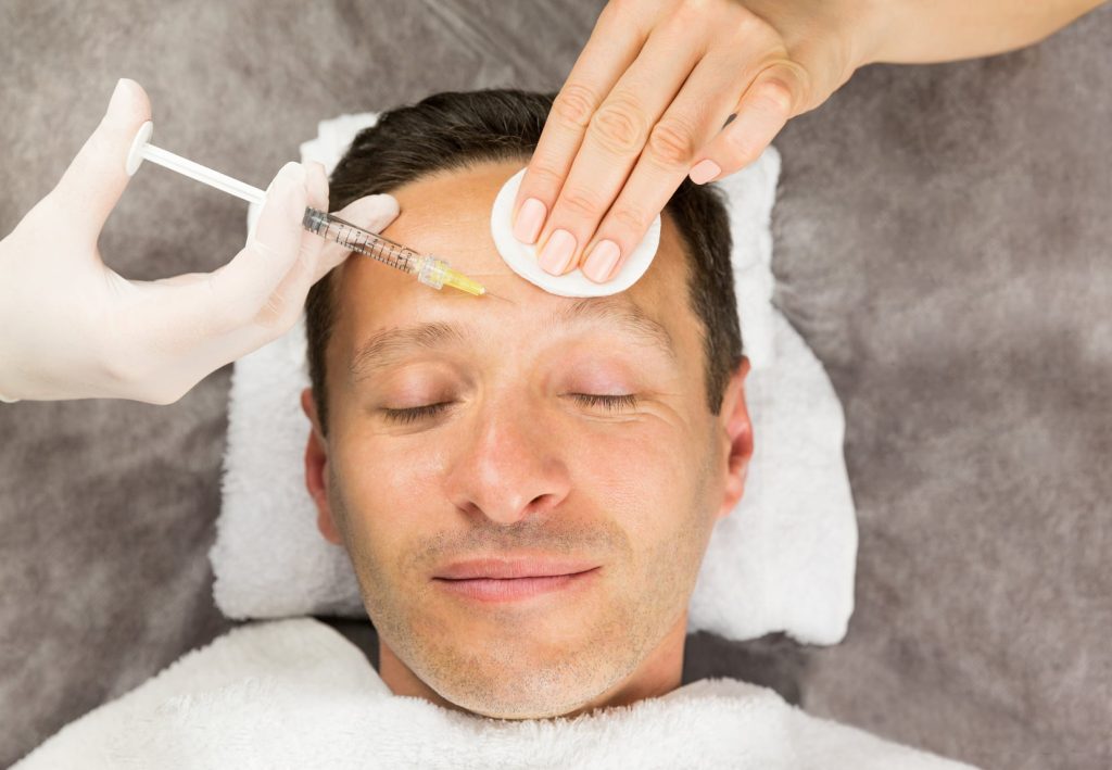Face of laying man, hands of beautician with a syringe and sponge, horisontal