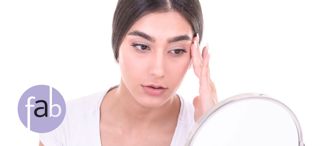 Atlanta area Woman looking into mirror and adjusting her eyebrow to see what a Brow Lift might look like post treatment.
